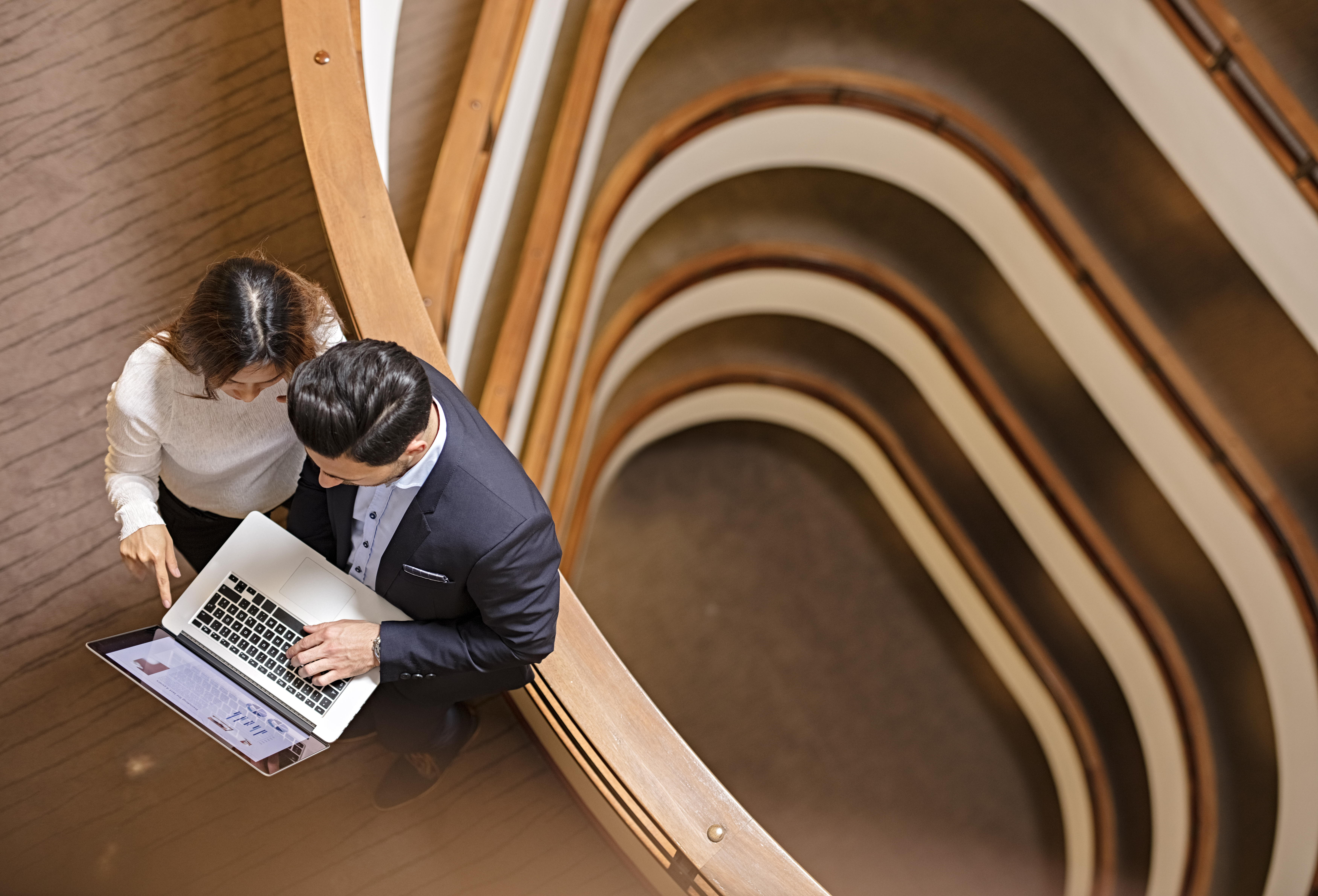 Two Business People Standing in the office building and Using Laptop